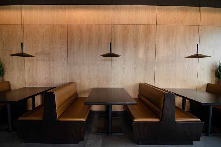 Light brown leather booths sit in front of a light wooden wall.