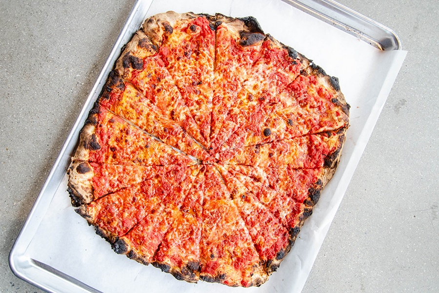 Overhead view of a cheese pizza on white paper on a metal tray.