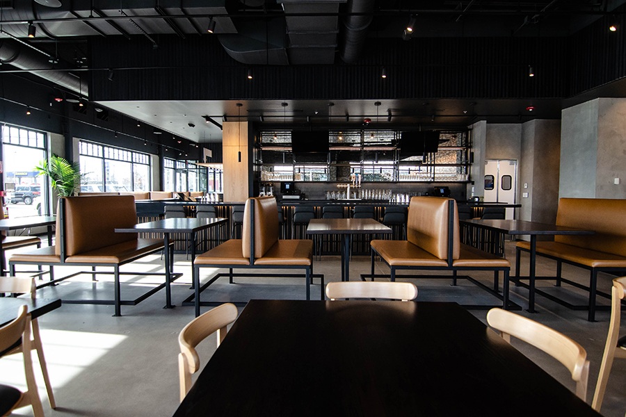 Interior view of a restaurant features light cement surfaces, light brown leather banquettes, and a sleek bar with black accents.