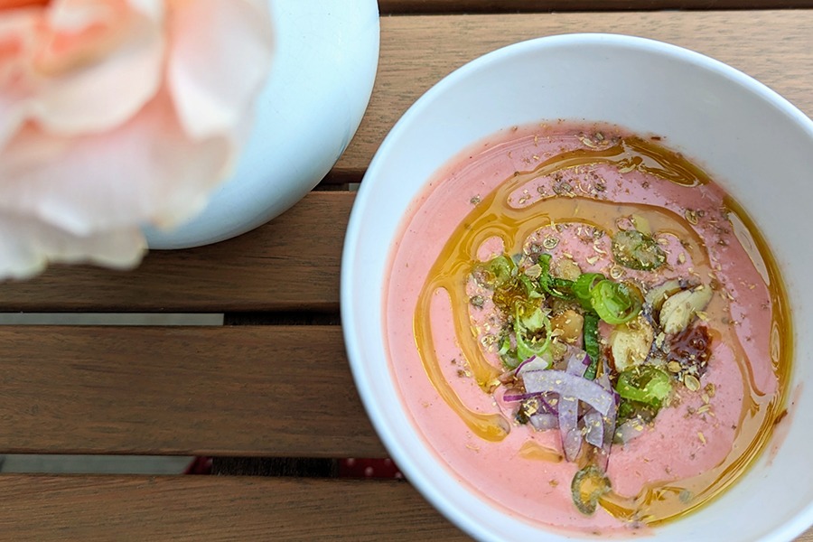 Overhead view of a bowl of thick pink soup with a swirl of olive oil and herbs.