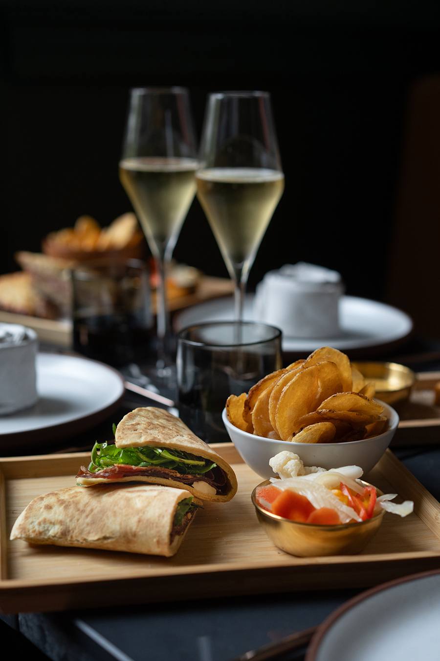 Meat, cheese, and greens are folded within pieces of flatbread, accompanied by potato chips and glasses of champagne.