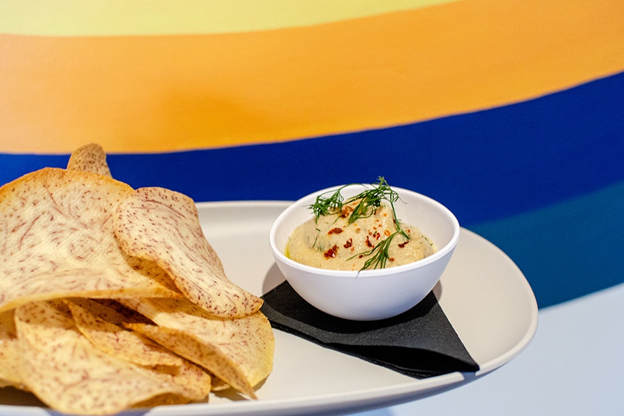 Round, thin chips made of taro sit on a plate next to a thick, creamy dip.