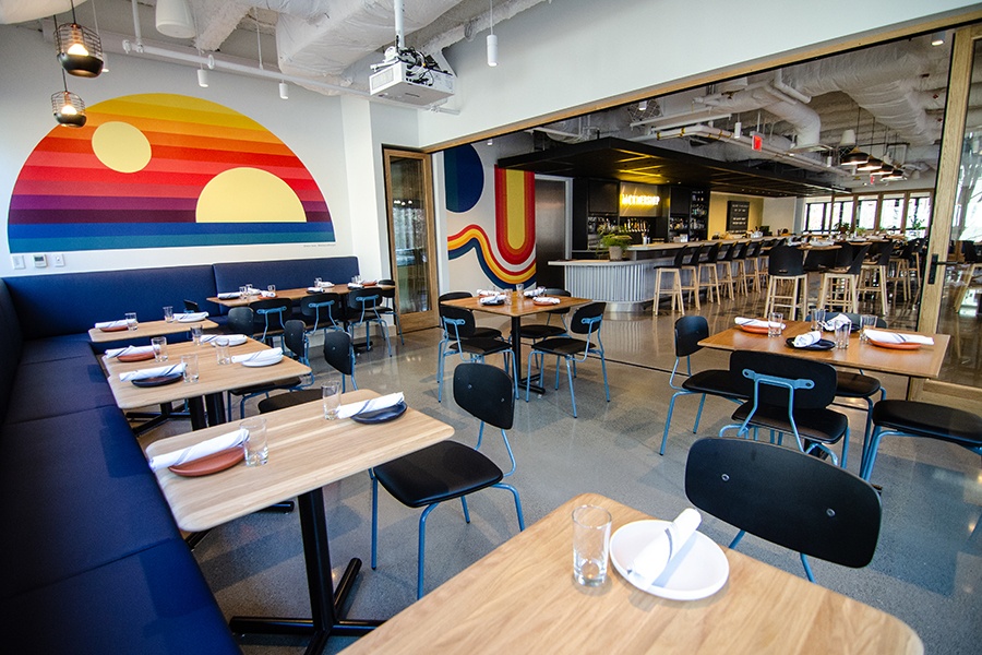 A restaurant interior features a royal blue banquette and colorful murals.