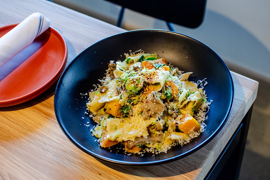 A dark plate holds thick pappardelle with ample parmesan and fall vegetables.