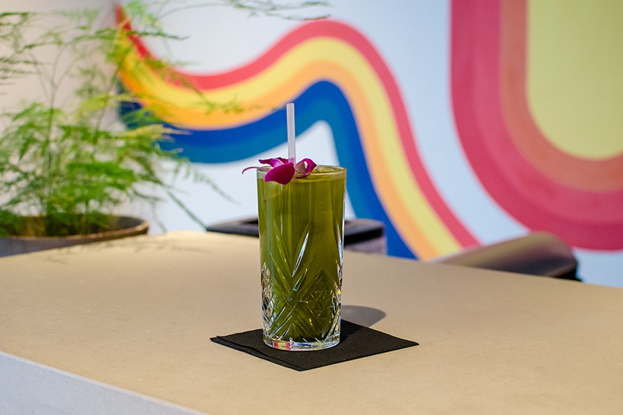 A green cocktail sits on a bar top in front of a rainbow-like mural.