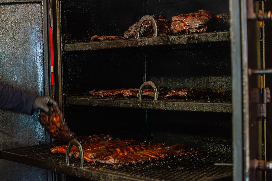 Pork butt, ribs, and other meat are visible inside a three-shelf smoker.