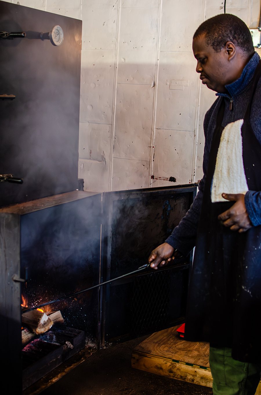 A man tends to a wood fire inside of a smoker.