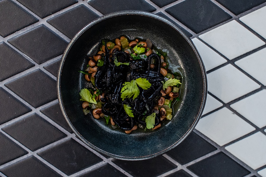 Squid tossed in jet black squid ink sits atop a bed of black-eyed peas in a black plate.