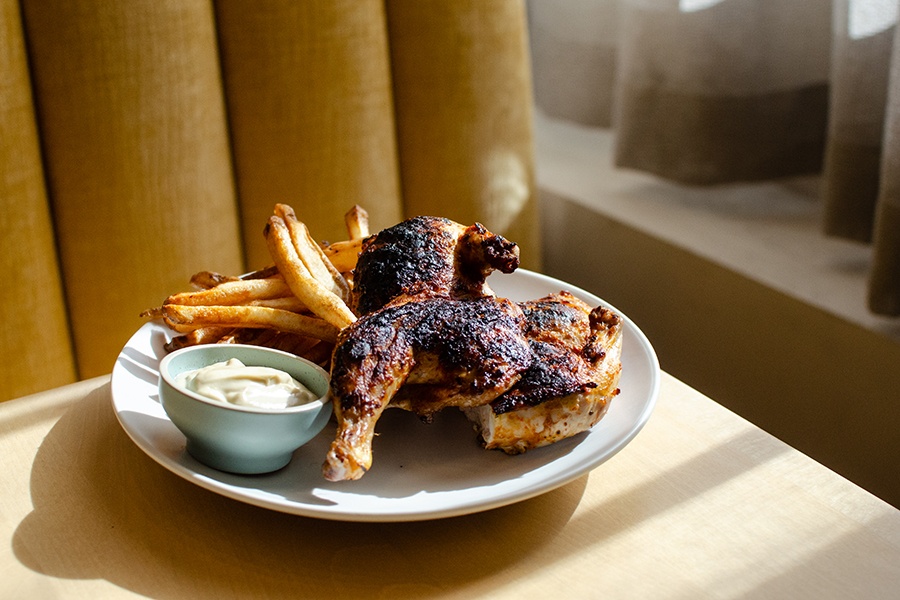 Grilled, spatchcocked chicken is accompanied by fries and a thick white sauce.