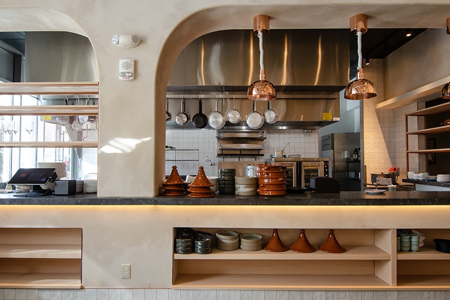 An empty restaurant kitchen features white tiling, gleaming pots and pans, and tagines.