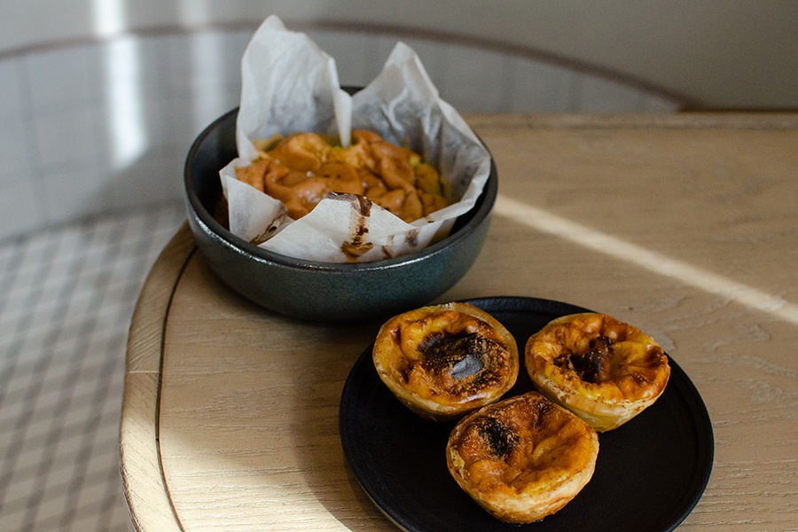 Three golden-brown egg tarts sit next to a soft sponge cake.