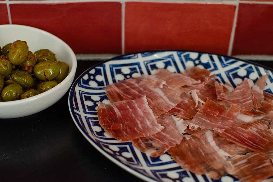 Thinly sliced fancy ham sits on a blue and white plate next to a side of green olives.