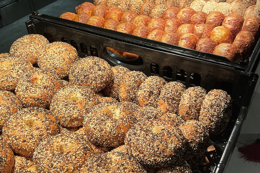 Two black bins are full of puffy bagels with various toppings.