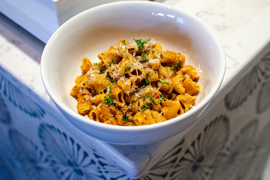Rigatoni in a Bolognese-style meat sauce sits in a white bowl on a marble countertop.