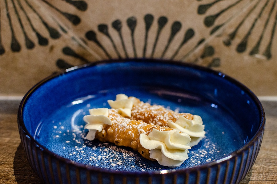 Two small cannoli sit on a blue plate, garnished with a light sprinkling of powdered sugar.
