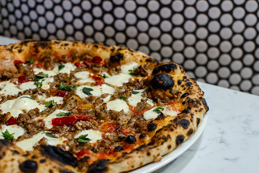 Closeup of a pizza with a leopard-spotted crust and a crumbled sausage topping, sitting on a white marble countertop.
