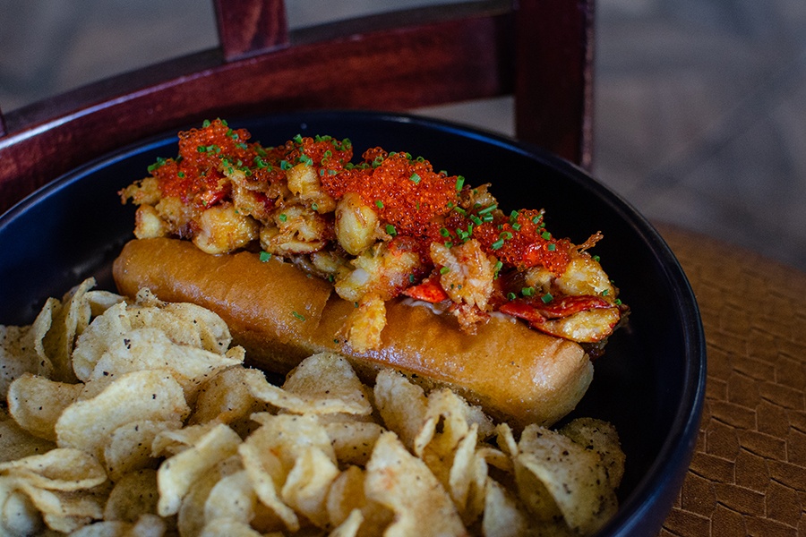 A buttery hot dog bun full of tobiko-topped fried lobster is accompanied by seasoned potato chips.