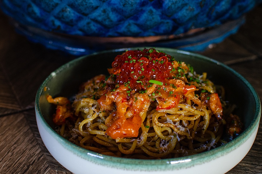 A green and white bowl holds noodles, crawfish, and salmon roe.