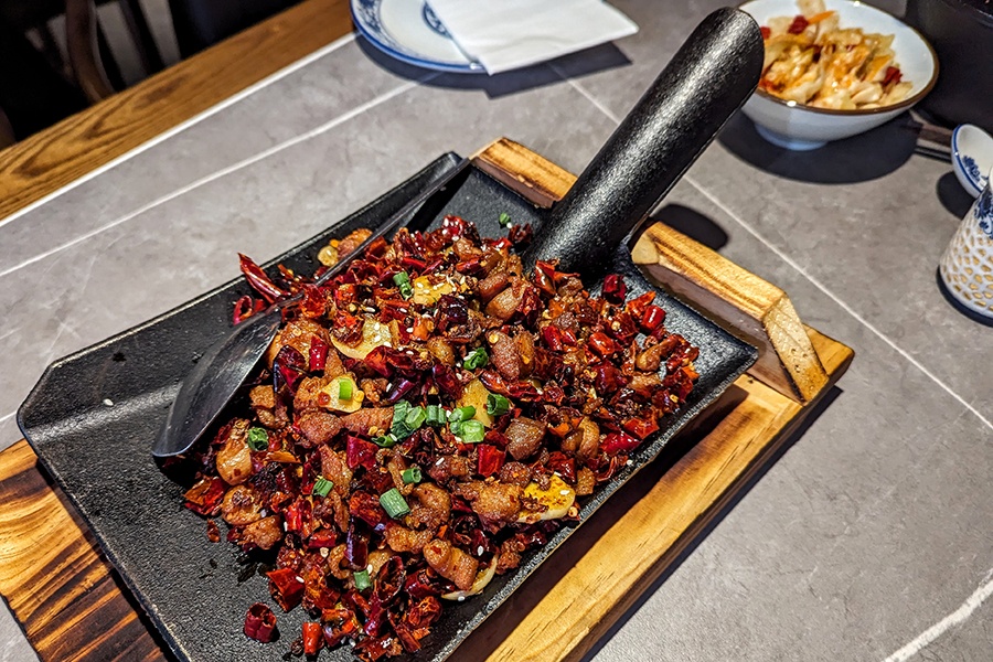 A cast-iron shovel-like plate is full of a Sichuan dish of stir-fried diced chicken and red peppers.