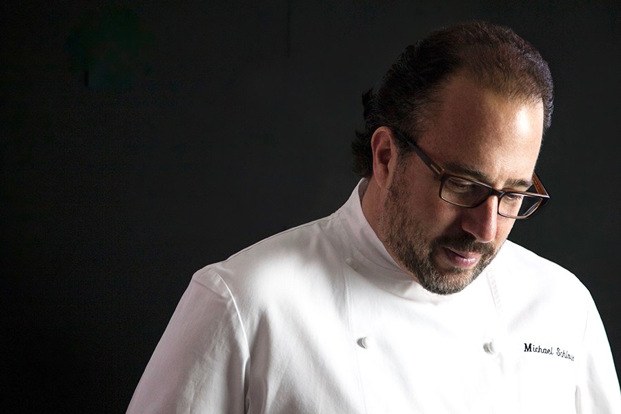 Headshot of a man with dark hair and a beard wearing chef's whites and glasses.