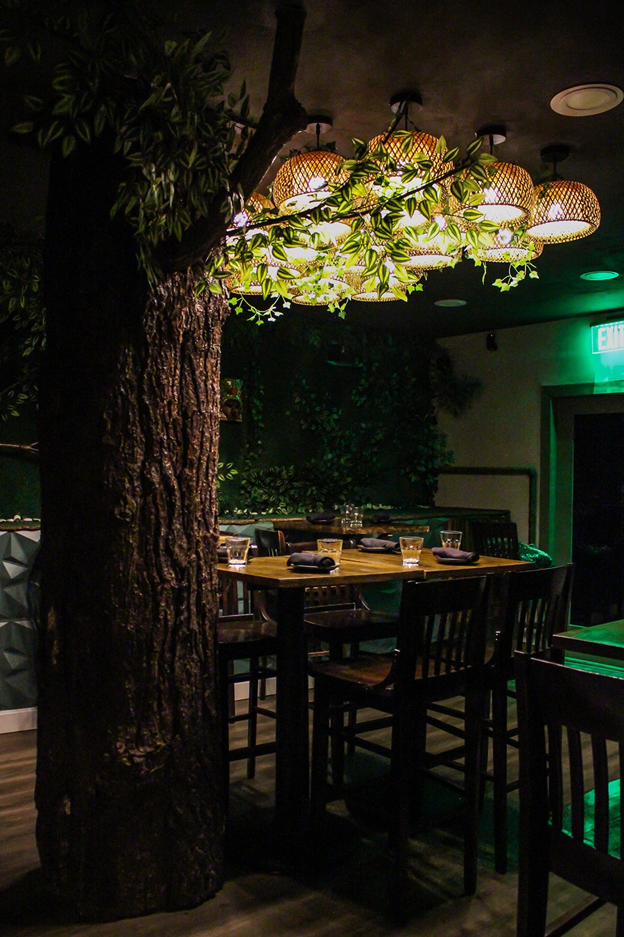 A restaurant's dining room features a large tree trunk and a greenery-covered wall.