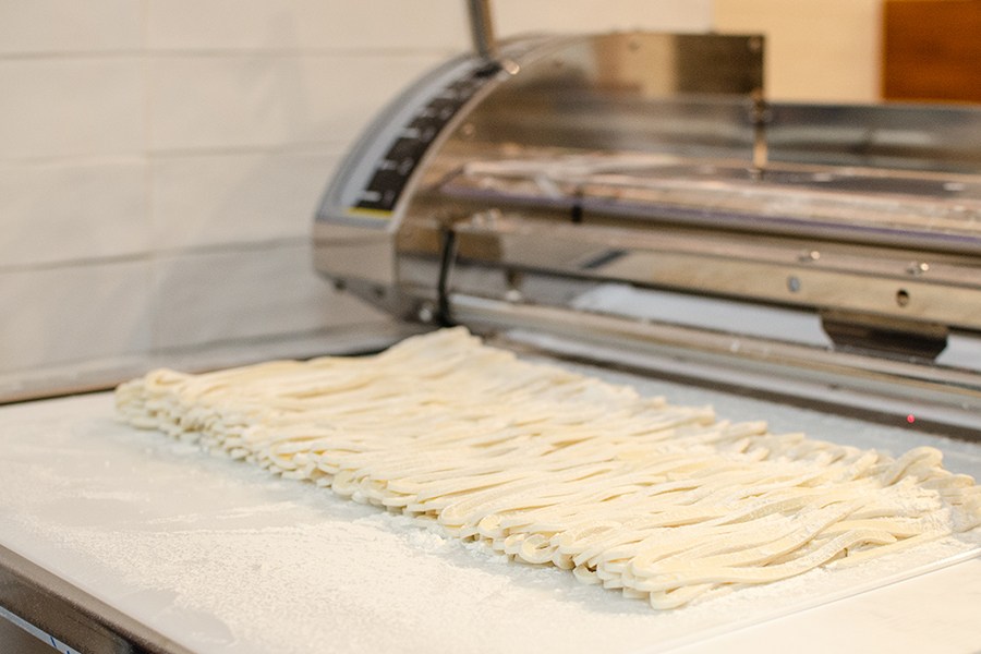Fresh udon noodles lined up in front of a commercial noodle-making machine.