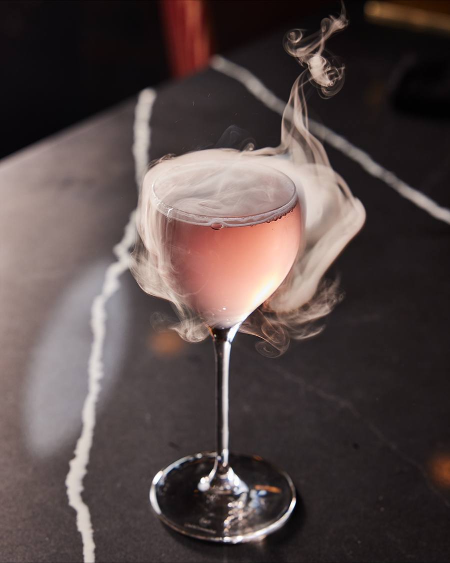 Smoke billows off of an elegant pink cocktail.