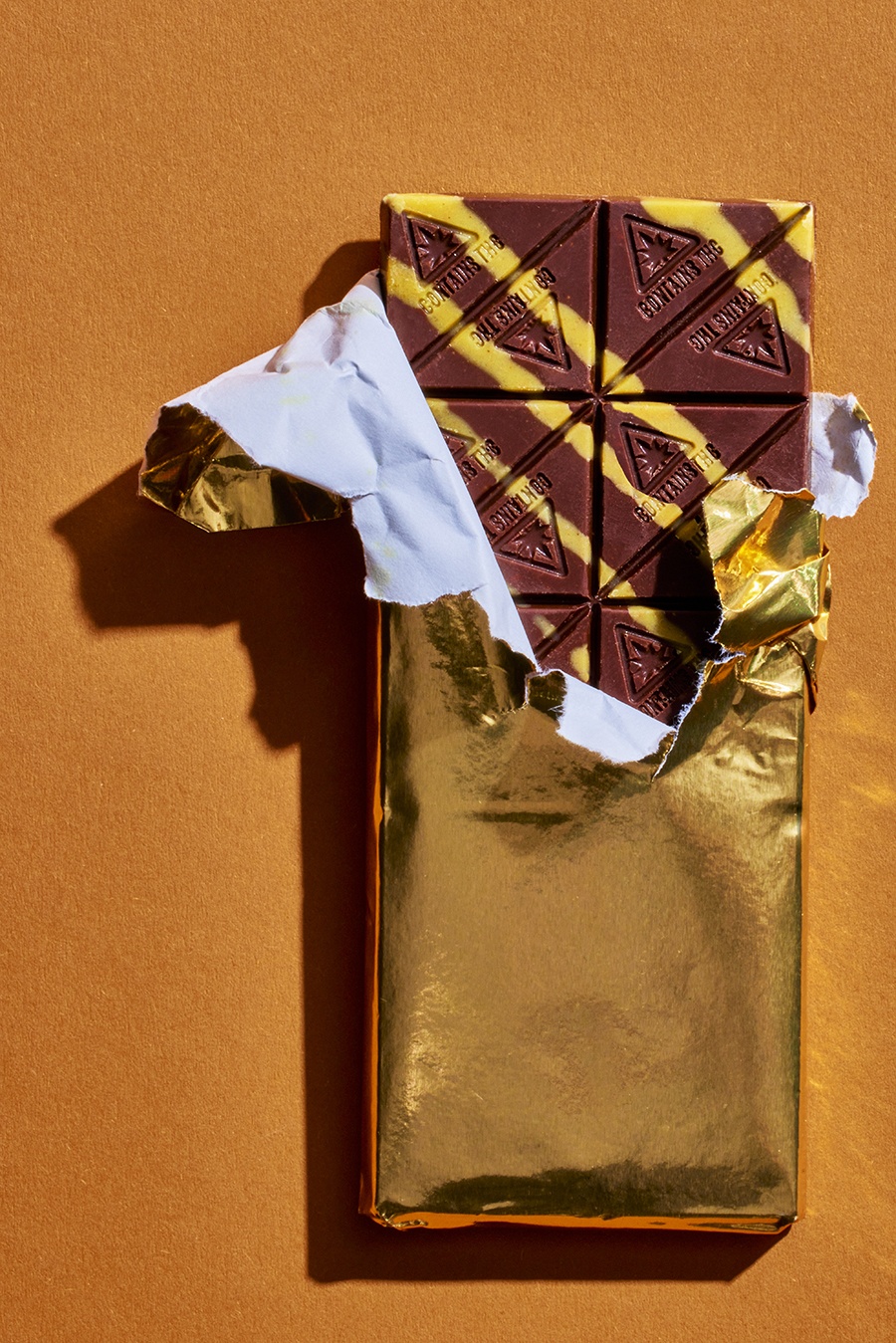 An infused chocolate bar with yellow stripes is shown in its partially opened golden wrapper.