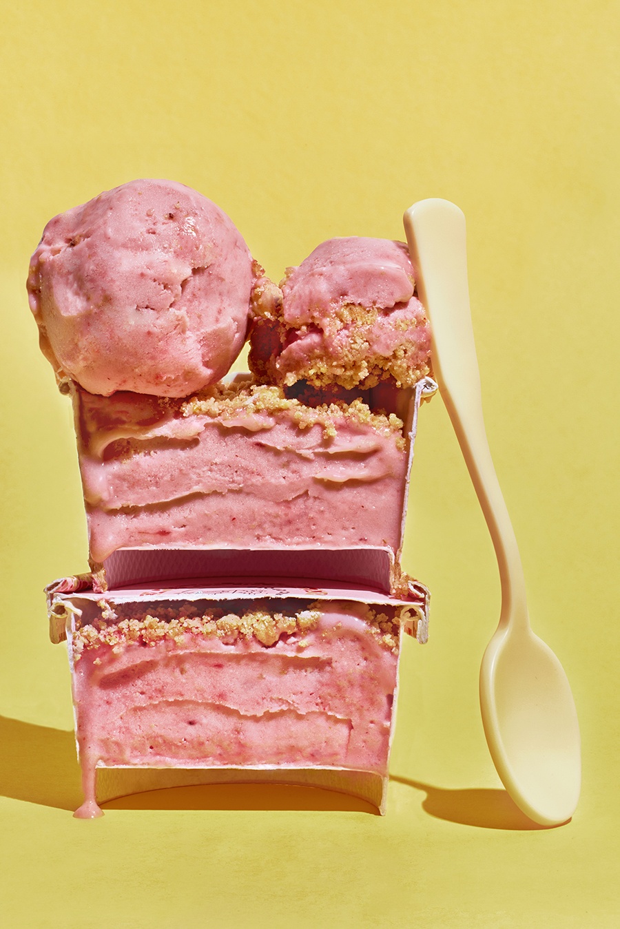 A small container of strawberry ice cream with a crumbly topping is cut in half, with one half stacked on top of the other, displaying the contents.