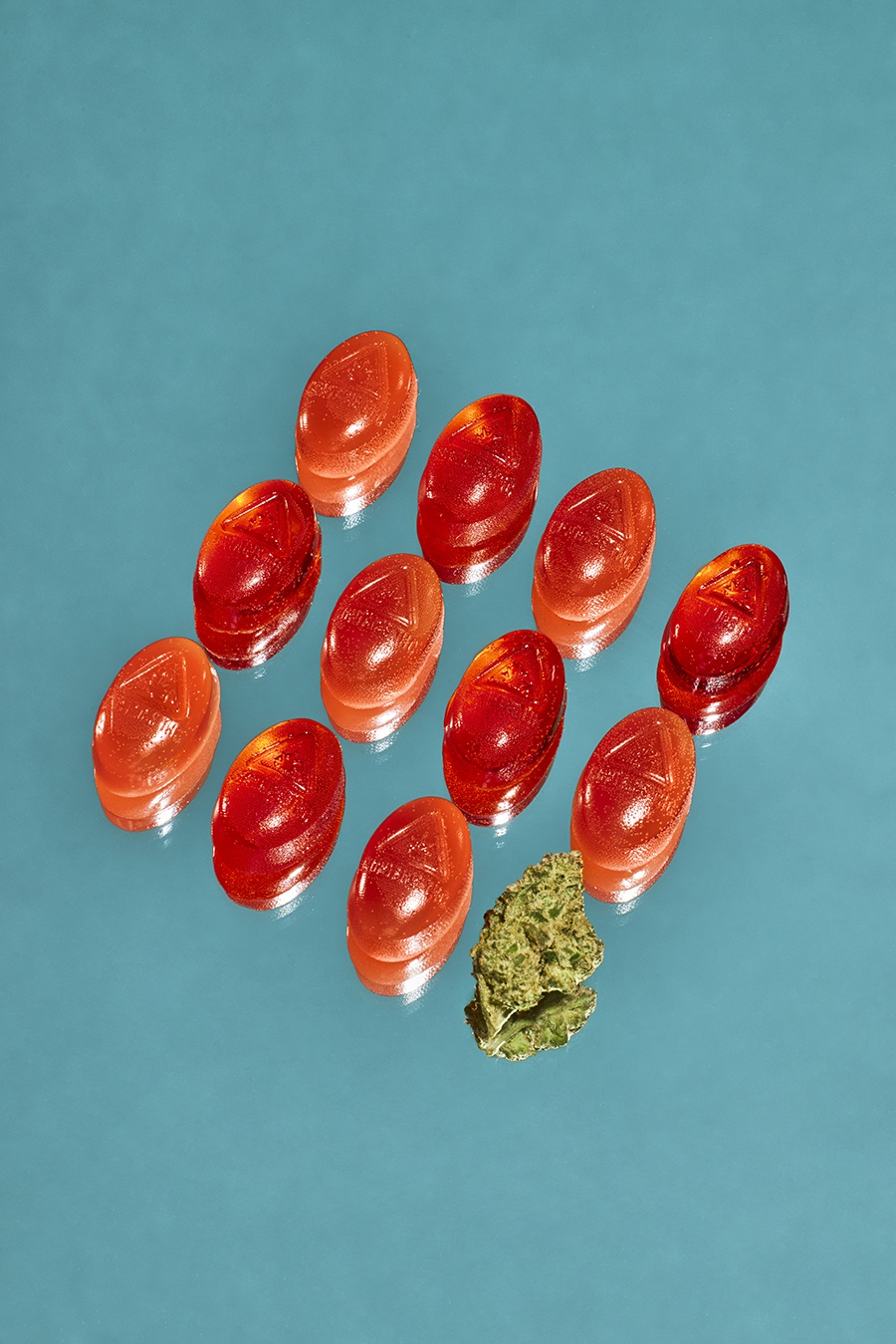 Red and orange infused gummies are displayed on a mirror next to a bit of cannabis.
