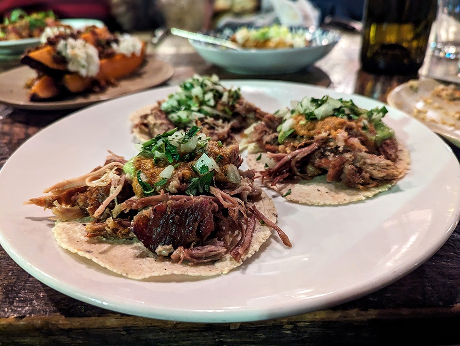 Three small tacos sit on a plate, topped with shredded pork, cilantro, and onions.