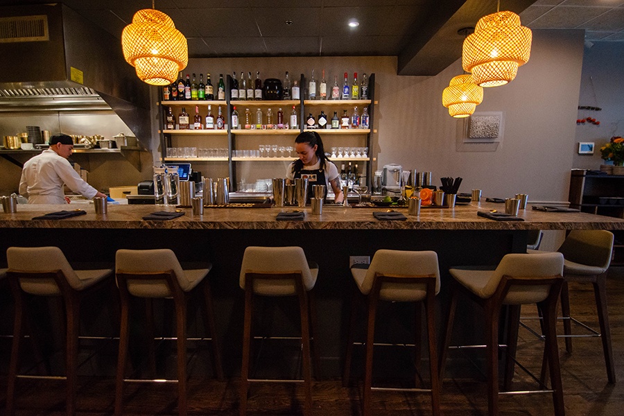 Restaurant staff work behind a marble bar in a restaurant with wicker light fixtures.