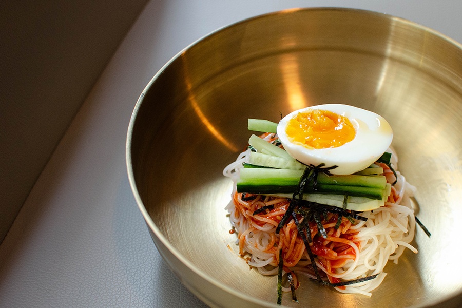 Half an egg sits atop sliced cucumber on a pile of white noodles with a red sauce.