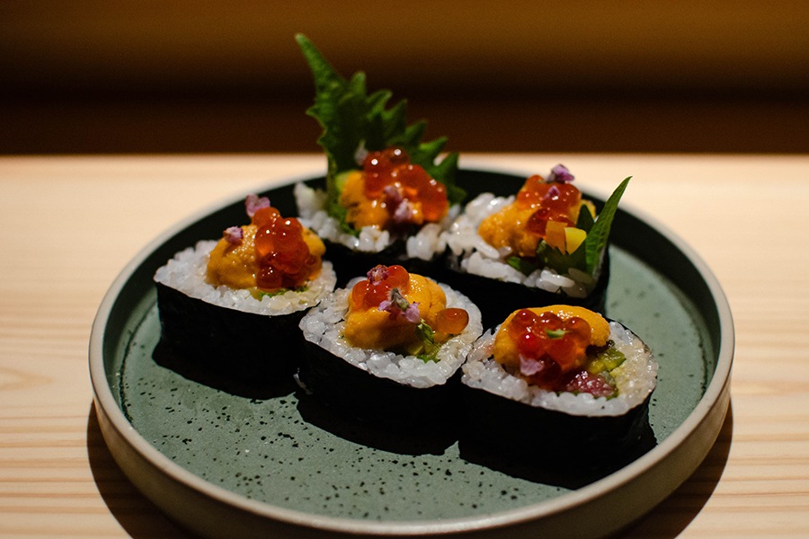 A sliced sushi roll is topped with ikura, uni, and more.