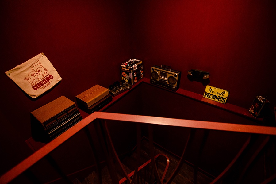 Music store paraphernalia is displayed on a shelf against a deep red wall along the stairway in a bar.