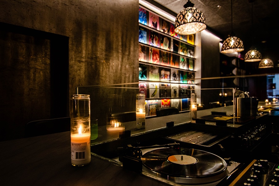 A record player and wall of records are displayed inside a dark bar.