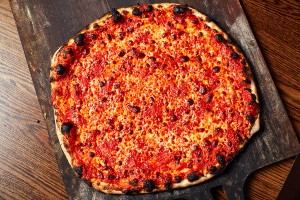 Overhead view of charred, thin-crust, New Haven-style pizza with tomato sauce and mozzarella.