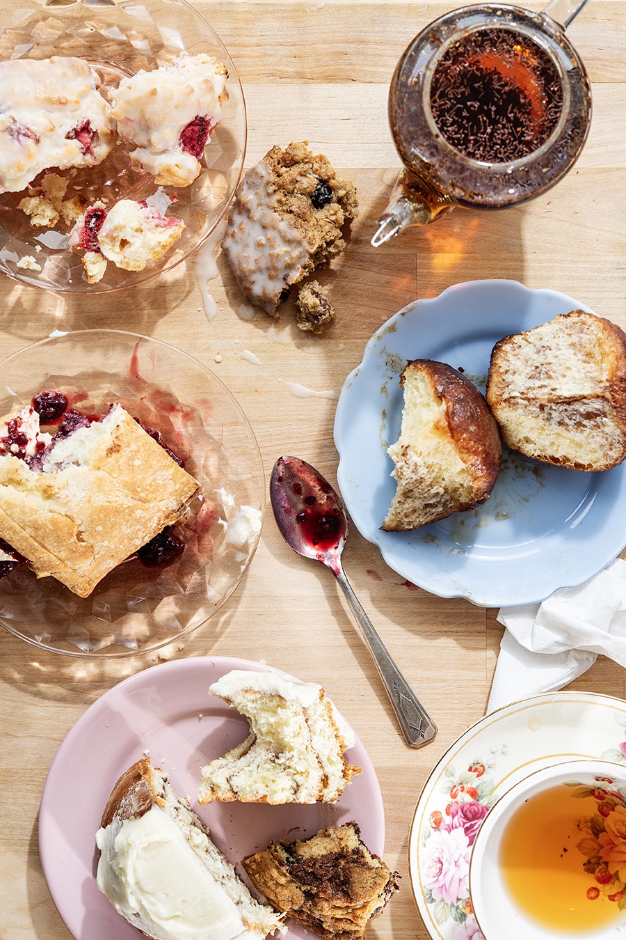 Overhead view of plates of partially eaten pastries, a floral cup of tea, and a glass teapot.