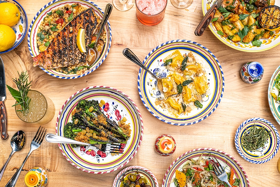 Overhead view of a light wooden table covered with colorful plates of food at an Italian restaurant.