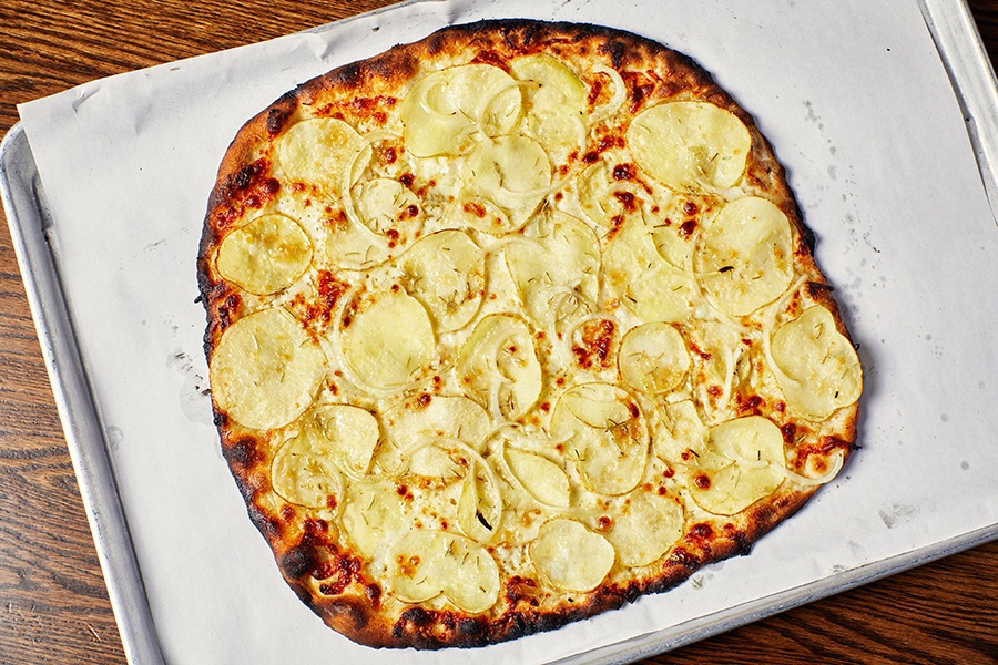 Overhead view of a thin, New Haven-style pizza topped with thinly sliced potatoes, onions, and rosemary.