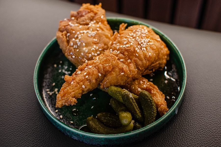 Crispy, glazed chicken pieces sit on a green plate with small pickles.