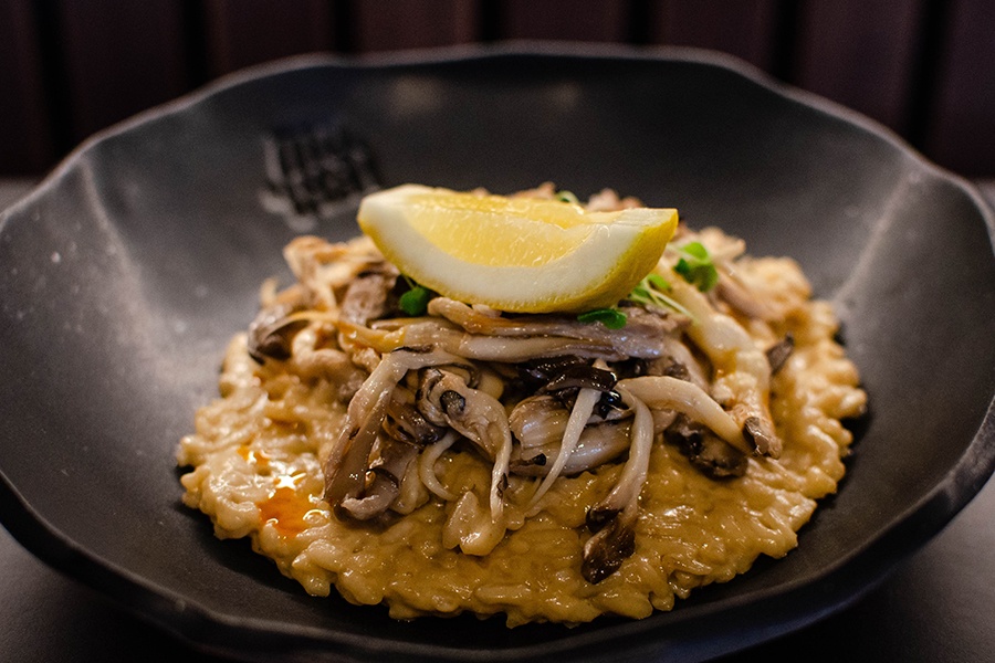 Thick risotto is topped with mushrooms and a lemon wedge.
