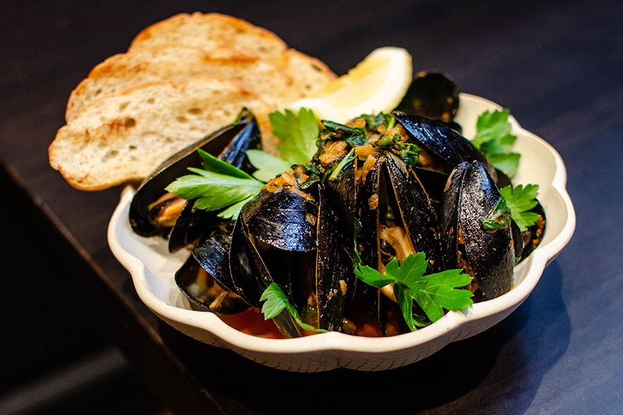 Steamed mussels are topped with cilantro and have a side of toasted bread.