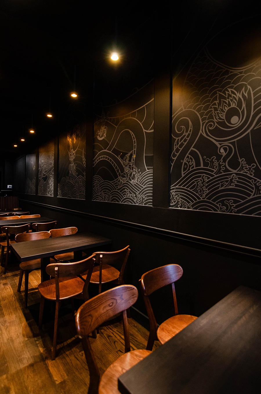 A dark restaurant dining room features a gray and gold mural of Thai-style figures and an ocean scene.
