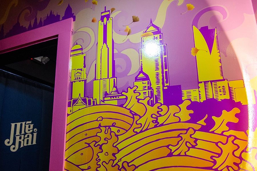 A restaurant bathroom mural features a yellow, purple, and orange cityscape.