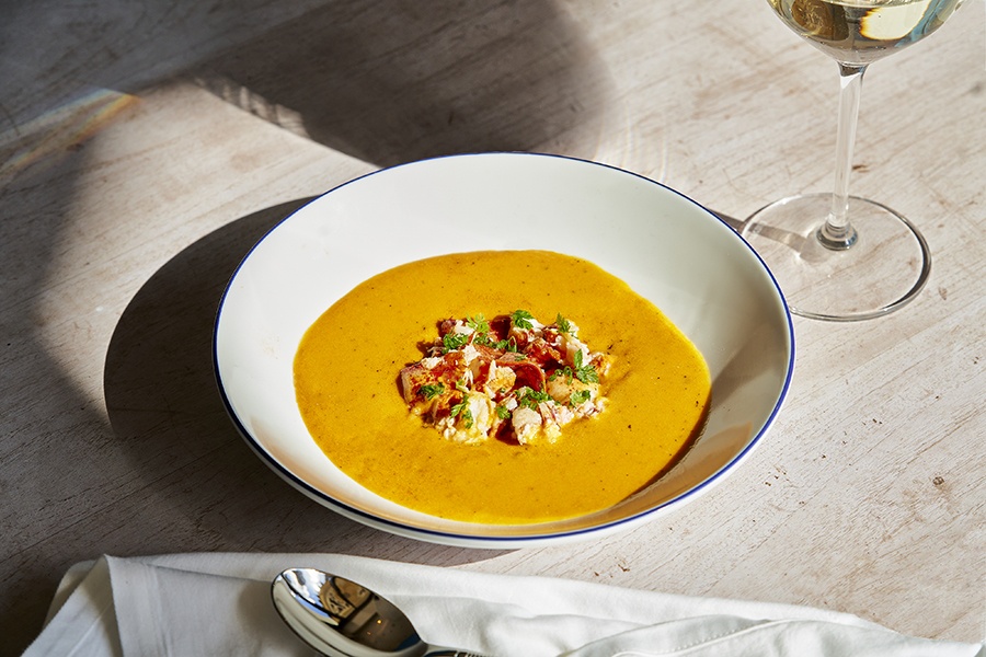 A white bowl is full of a thick, pale orange bisque topped with pieces of lobster.