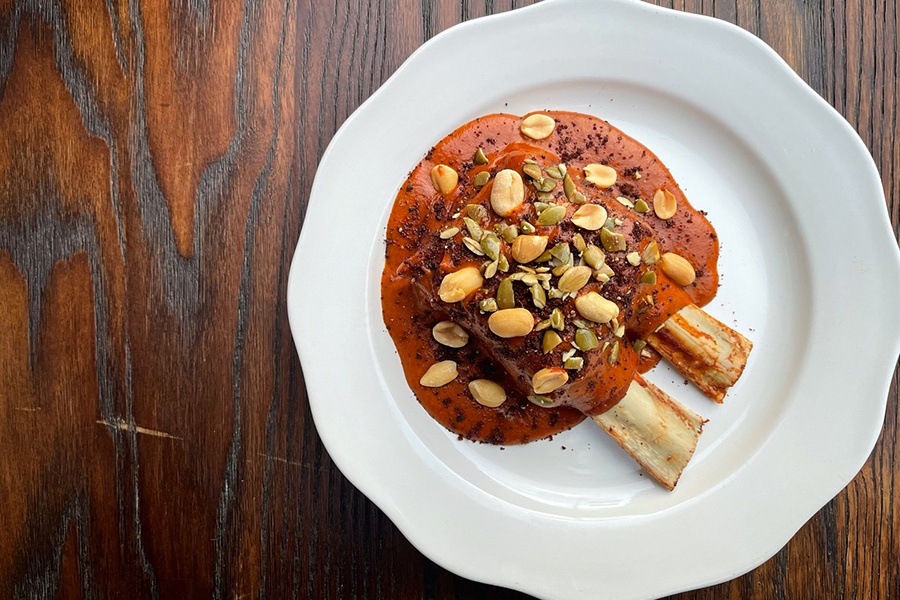 Overhead view of meaty ribs in an orange-brown sauce, garnished with pepitas and peanuts.