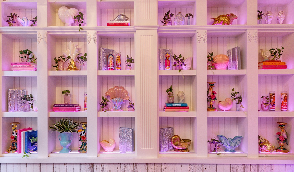 A white restaurant wall with pink lighting of shelving with trinkets