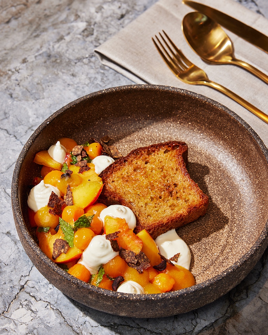 Overhead view of a piece of toasted bread with nectarines, yellow tomatoes, herbs, and dollops of a soft cheese.