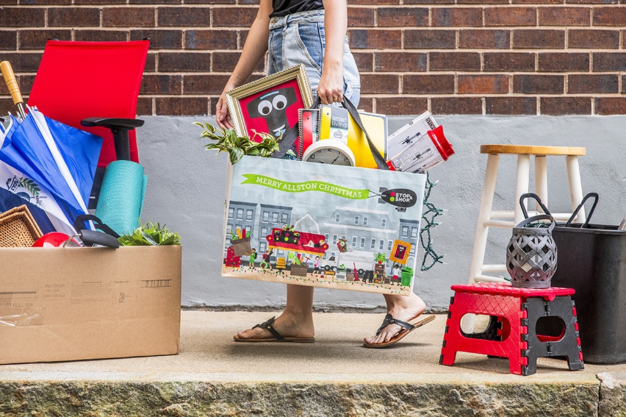 A person carries a shopping bag stuffed with school supplies. The bag says "Merry Allston Christmas."